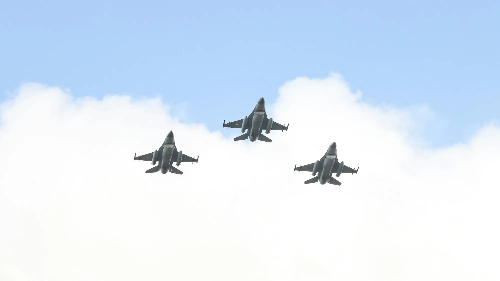 Three fighter jets flying in formation above the clouds